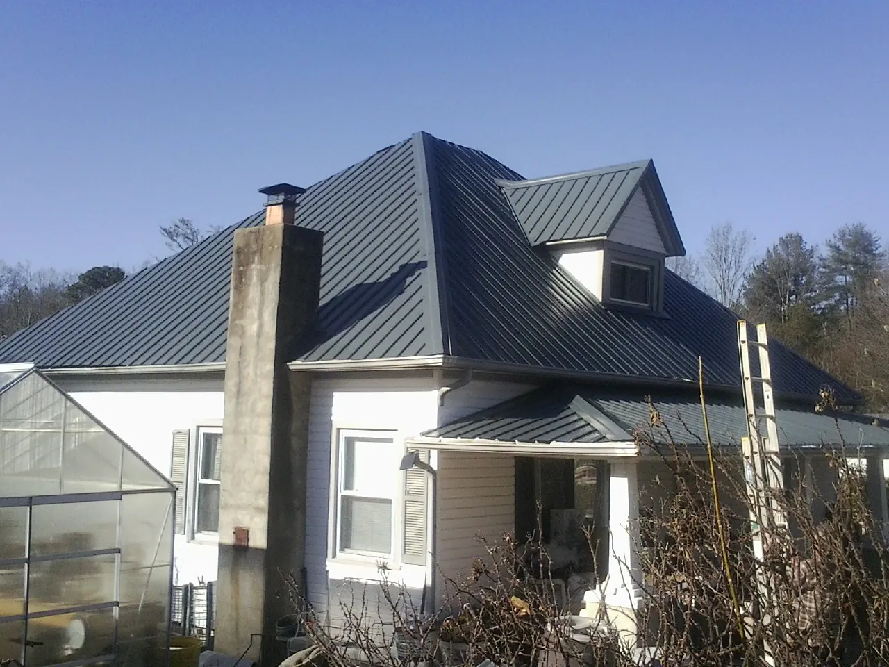 Dark blue standing seam metal roof on a white farmhouse with dormer — Slate & Tile Roof Repair by Roofing Brothers in Pittsford