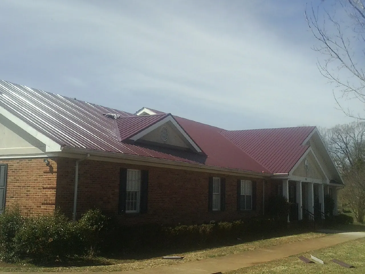 Red metal roof with gabled entries on a long brick building, from a Hail Damage Roof Repair job in Pittsford