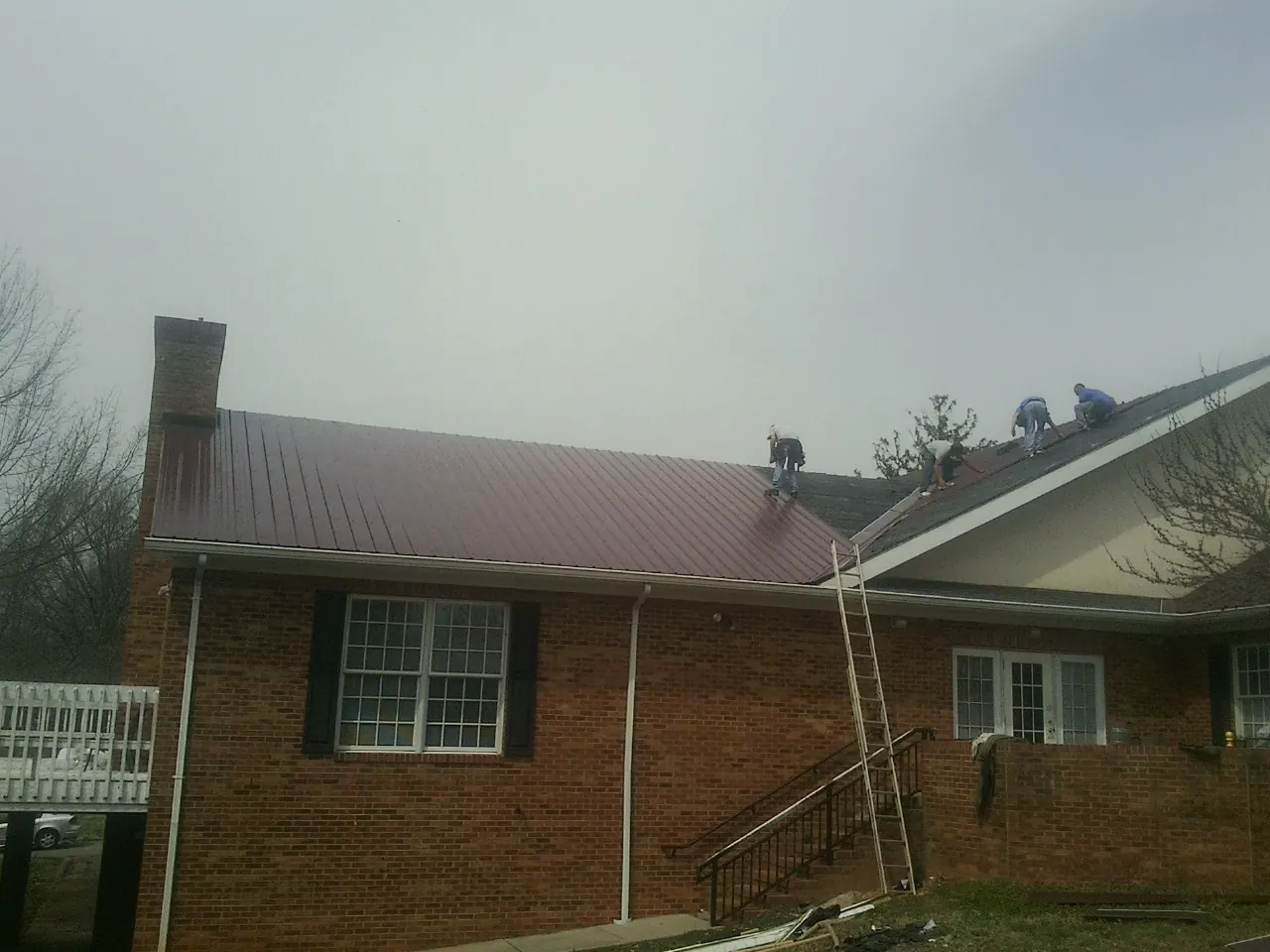 Crew setting red metal roofing panels on a brick home in Pittsford