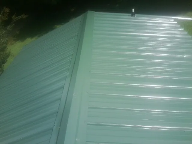 New green metal panels meeting at the ridge of a roof — Flat Roof Repair work by our crew in Pittsford