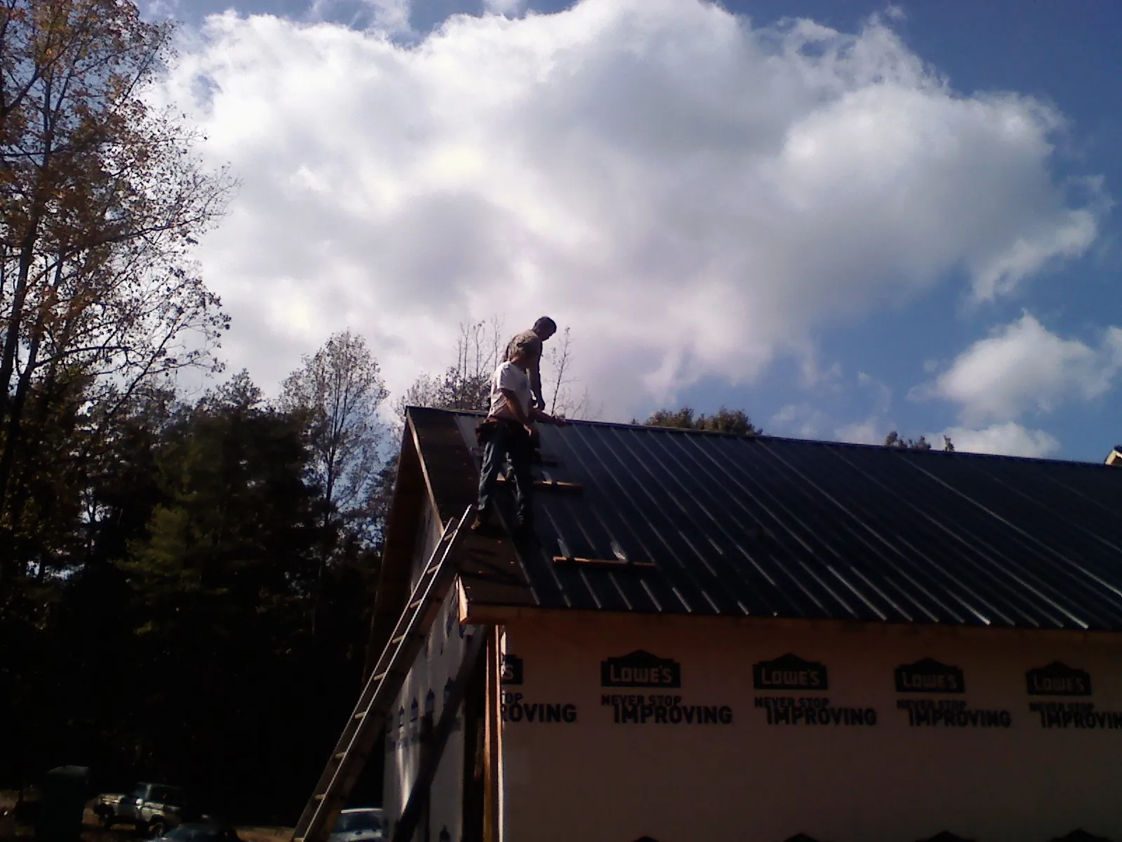 Roofer fastening dark metal panels high against a cloudy sky, from a Roof Inspection job in Pittsford
