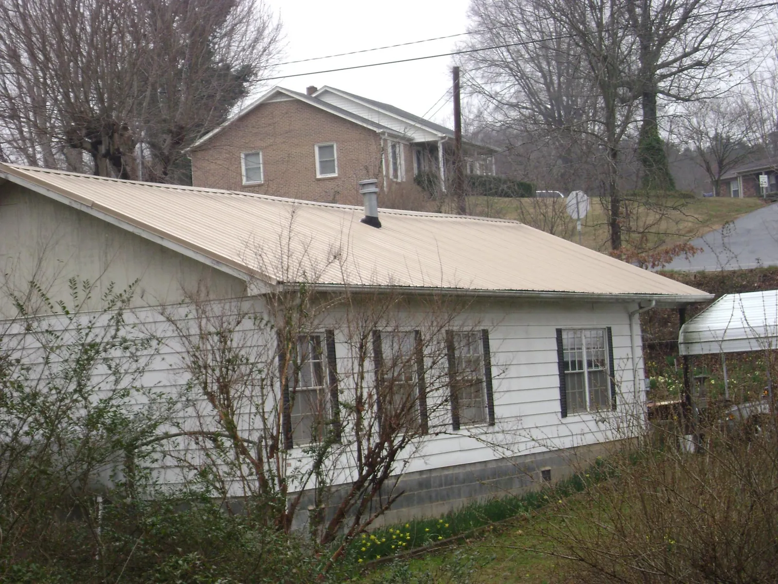 Tan metal roof on a white sided house set into a hillside — Commercial Roofing by Roofing Brothers in Pittsford