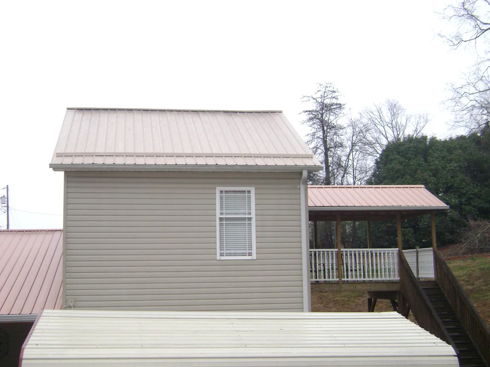 Tan metal roofs on a two story addition and attached porch, from a Roof Replacement job in Pittsford